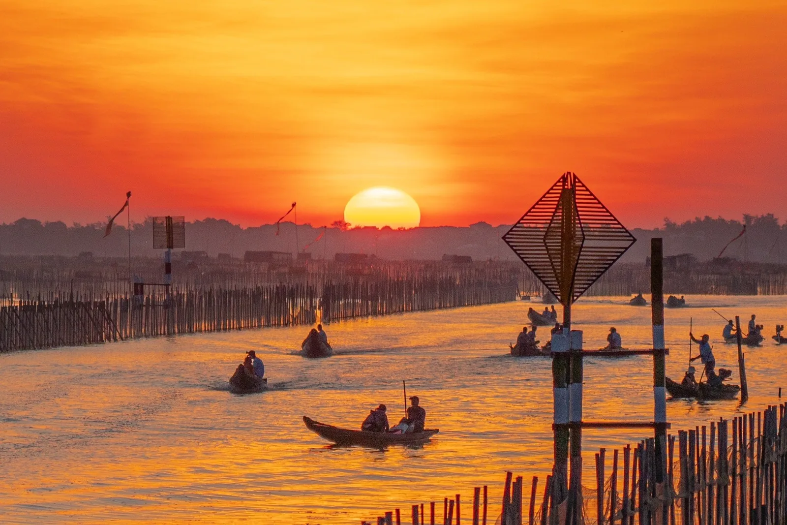 Small wooden boats glide across a river lagoon near Hue as the sun sets in a blazing orange sky.