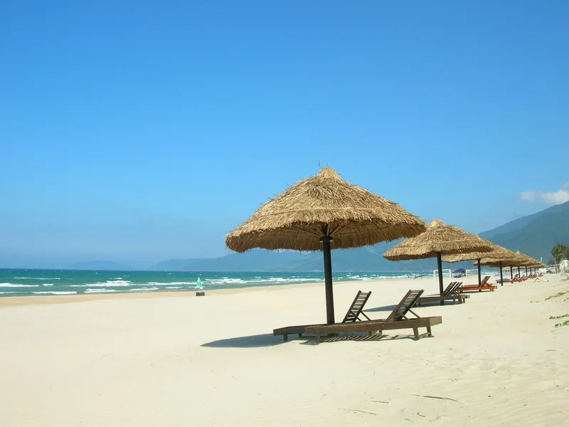 Thatched umbrellas and lounge chairs line the sandy shore of Lang Co Beach in Hue, Vietnam.