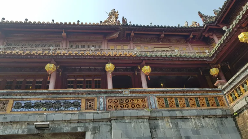 Ornate wooden façade with yellow lanterns and ceramic tile decoration at Dien Tho Palace in Hue's Imperial City.