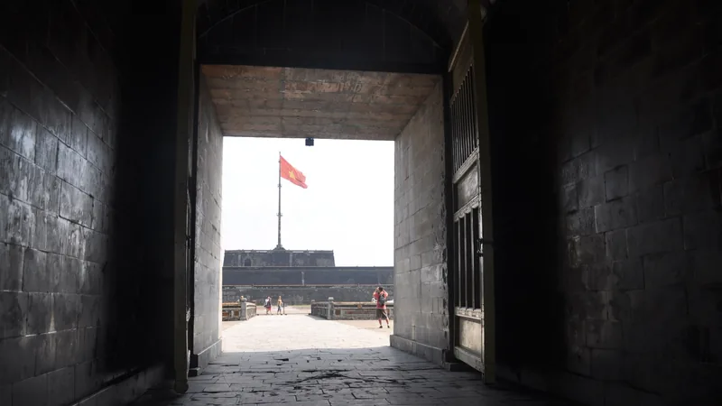 A dark stone archway frames a view of the Vietnamese flag flying over the Imperial City in Hue.