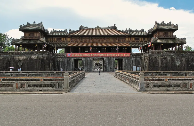The Ngo Mon Gate entrance to Hue's Imperial City, with its bridge and tiered pavilion roof, under a partly cloudy sky.