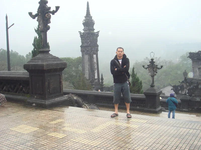 A visitor stands on the misty terrace of Khai Dinh Tomb amid ornate stone towers in Hue.