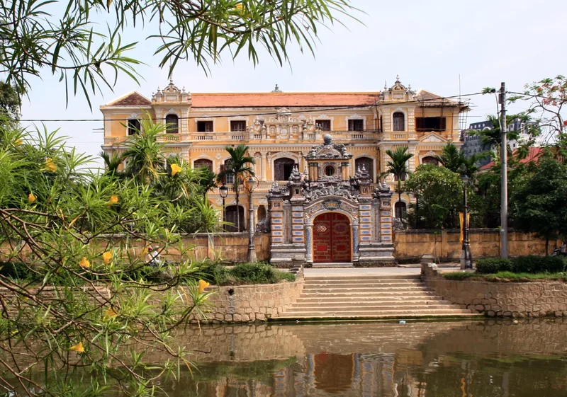 An Dinh Palace's ornate French-colonial facade rises behind a pond and flowering shrubs in Hue, Vietnam.