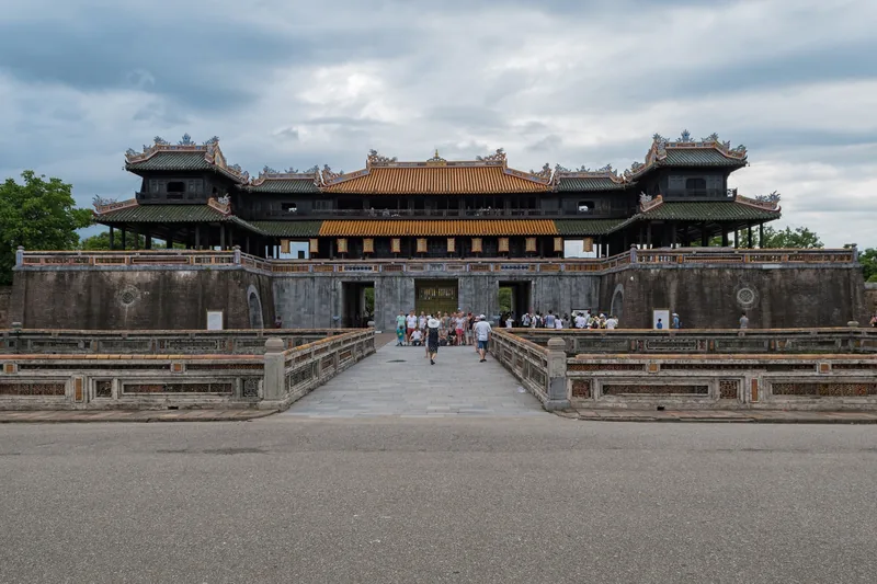 Visitors approach the Ngo Mon Gate entrance to the Hue Citadel under a cloudy sky.