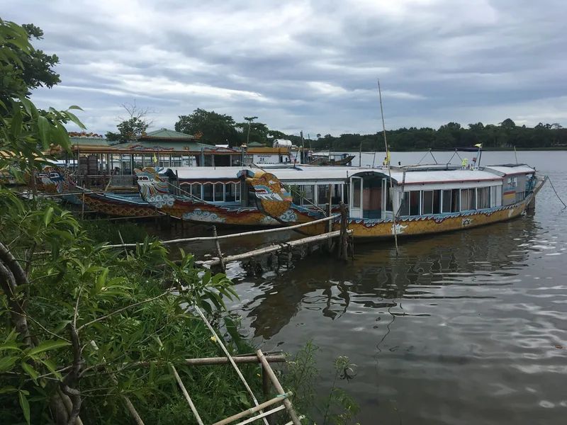 Colorful dragon boats moored along the Perfume River in Hue under a cloudy sky.