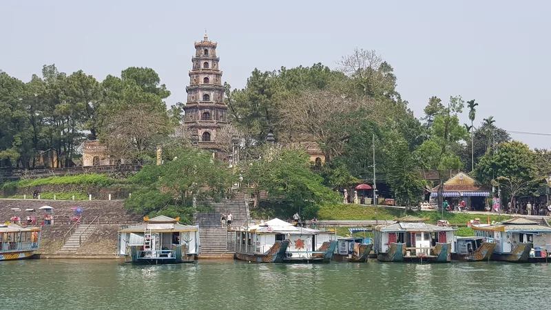 The seven-tiered Thien Mu Pagoda rises above the Perfume River with dragon boats moored along the bank in Hue.