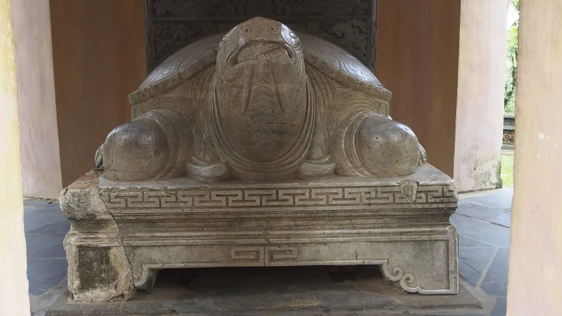 A stone turtle statue carved with intricate patterns stands beneath a pavilion at Thien Mu Pagoda in Hue.
