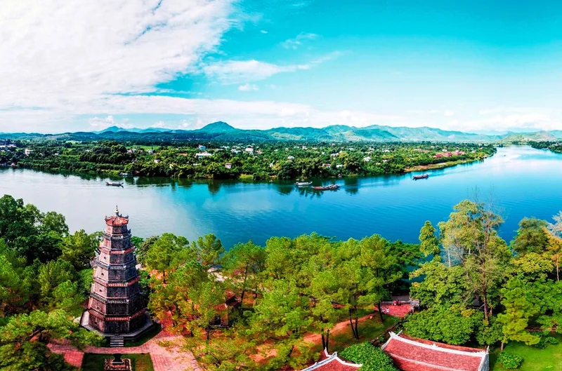 Aerial view of the Thien Mu Pagoda tower beside the Perfume River winding through green hills in Hue.