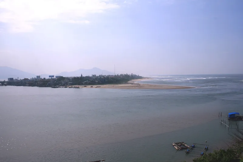 A river meets the sea at a sandy spit near Lang Co, Hue, with distant mountains and small boats.