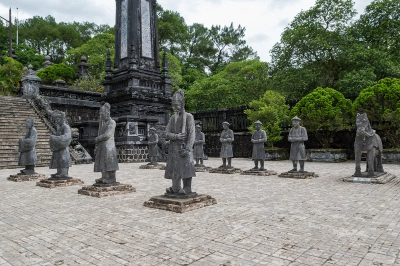 Rows of stone mandarin and horse statues stand before an obelisk at Khai Dinh Tomb in Hue.