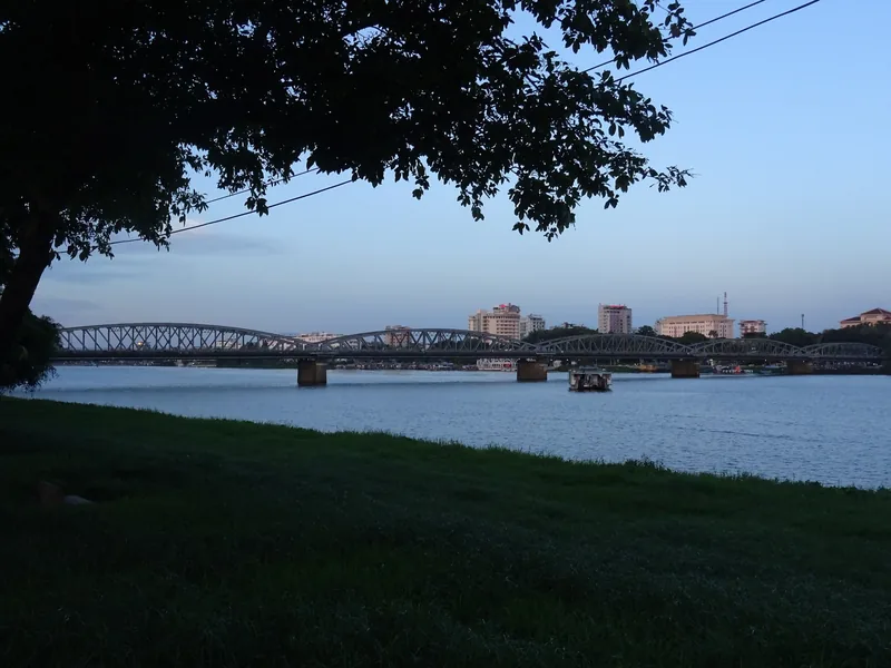 Truong Tien Bridge spans the Perfume River at dusk, framed by a riverside tree in Hue.