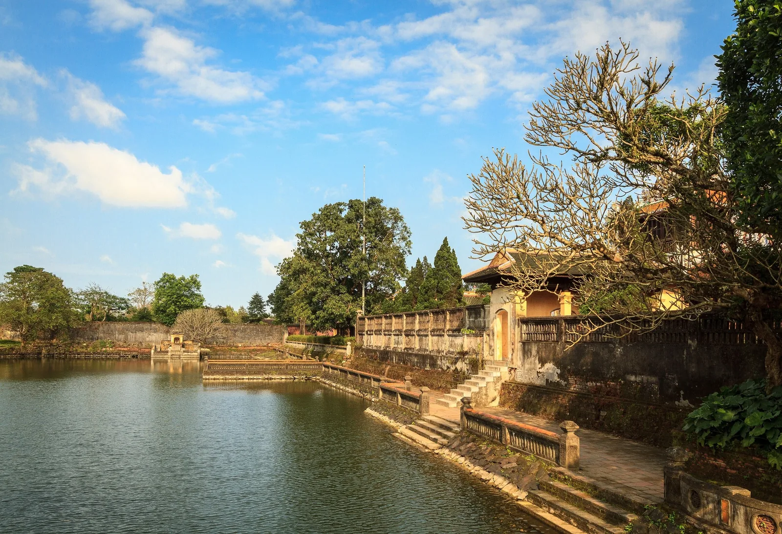 Stone steps lead down to a tranquil moat beside weathered walls of the Hue Imperial City.